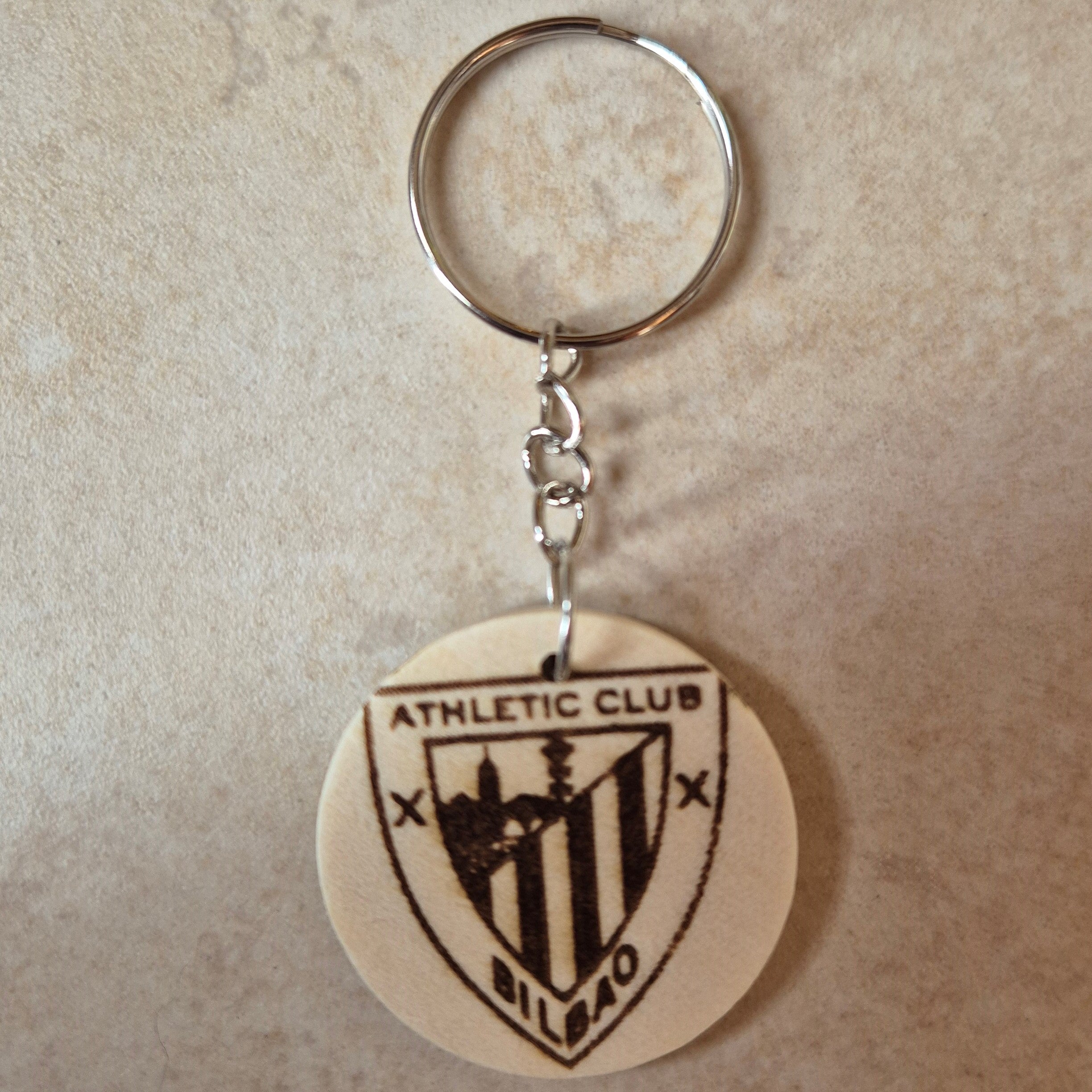 Llavero artesanal fabricado en madera natural, cortado y grabado mediante tecnología láser de alta precisión.

Presenta un diseño circular de acabado suave, con grabado permanente de gran definición que resalta el escudo del Athletic Club de Bilbao con un contraste elegante y duradero.

Incluye resistente aro metálico con cadena, ideal para llaves, mochilas...

Gracias a su ligereza y estilo natural, es perfecto como regalo personalizado o detalle ecológico.

Grabado a doble cara.

¡Contacta con nosotros pa