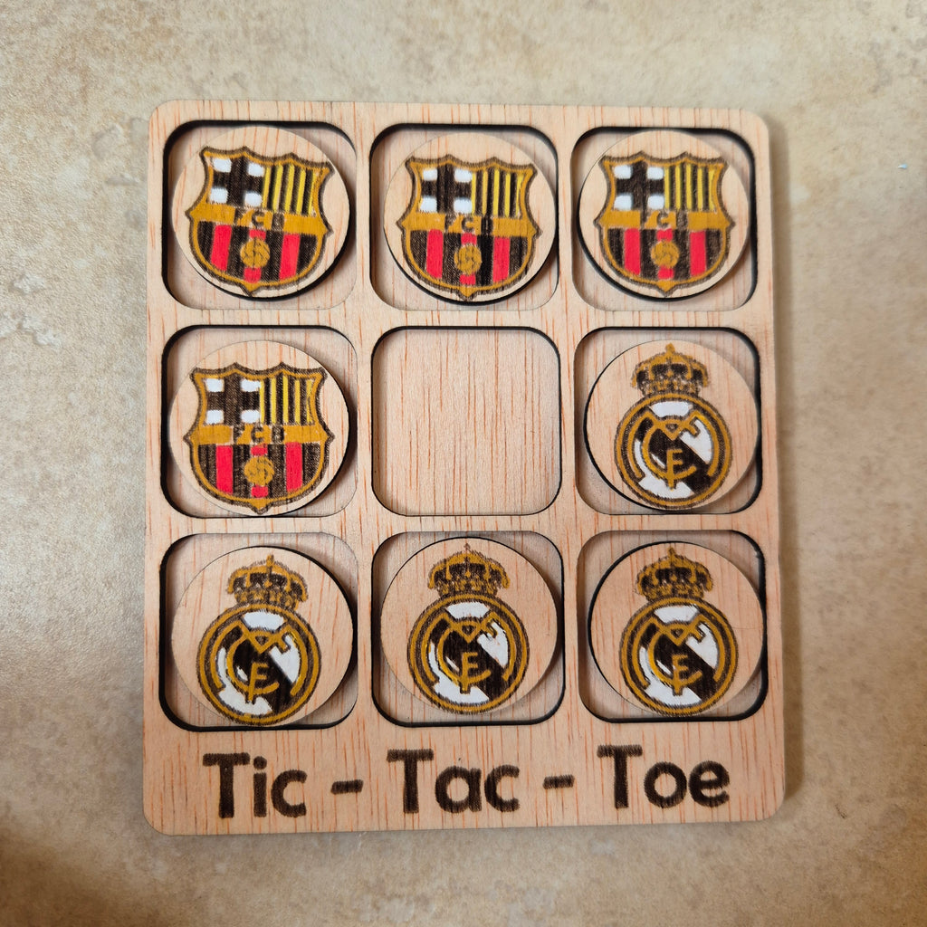 Hermoso juego de Tic-Tac-Toe (Tres en raya) artesanal, elaborado en madera natural mediante técnica de corte y grabado láser, y pintado completamente a mano con gran detalle y cuidado.

Incluye fichas ilustradas con los mejores equipos de España (F. C. Barcelona y Real Madrid), lo que lo convierte en un artículo único, colorido y lleno de encanto, ideal tanto para jugar como para decorar.

Perfecto como regalo original, recuerdo artesanal o elemento decorativo para habitaciones infantiles, escritorios o est