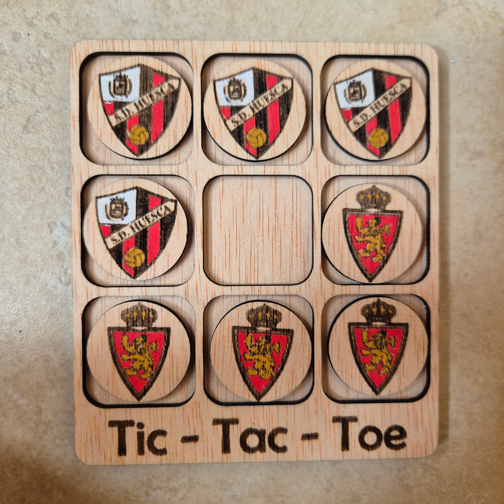 Hermoso juego de Tic-Tac-Toe (Tres en raya) artesanal, elaborado en madera natural mediante técnica de corte y grabado láser, y pintado completamente a mano con gran detalle y cuidado.

Incluye fichas ilustradas con los fantásticos clubs de fútbol de Aragón (S. D. Huesca y Real Zaragoza), lo que lo convierte en un artículo único, colorido y lleno de encanto, ideal tanto para jugar como para decorar.

Perfecto como regalo original, recuerdo artesanal o elemento decorativo para habitaciones infantiles, escrit