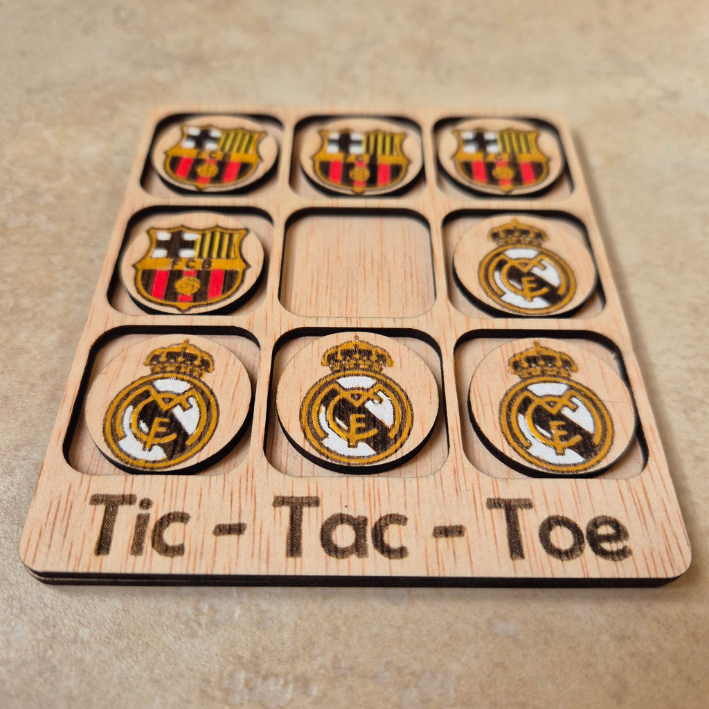 Hermoso juego de Tic-Tac-Toe (Tres en raya) artesanal, elaborado en madera natural mediante técnica de corte y grabado láser, y pintado completamente a mano con gran detalle y cuidado.

Incluye fichas ilustradas con los mejores equipos de España (F. C. Barcelona y Real Madrid), lo que lo convierte en un artículo único, colorido y lleno de encanto, ideal tanto para jugar como para decorar.

Perfecto como regalo original, recuerdo artesanal o elemento decorativo para habitaciones infantiles, escritorios o est