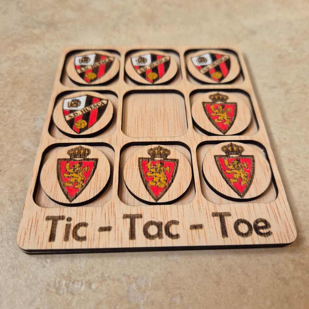 Hermoso juego de Tic-Tac-Toe (Tres en raya) artesanal, elaborado en madera natural mediante técnica de corte y grabado láser, y pintado completamente a mano con gran detalle y cuidado.

Incluye fichas ilustradas con los fantásticos clubs de fútbol de Aragón (S. D. Huesca y Real Zaragoza), lo que lo convierte en un artículo único, colorido y lleno de encanto, ideal tanto para jugar como para decorar.

Perfecto como regalo original, recuerdo artesanal o elemento decorativo para habitaciones infantiles, escrit
